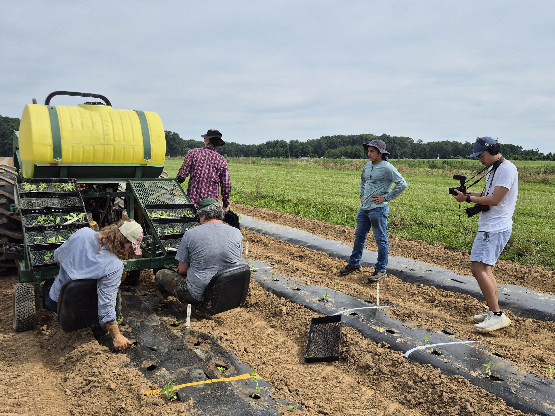 Cinematographer Evan recording graduate students planting young basil plants on the back of a tractor